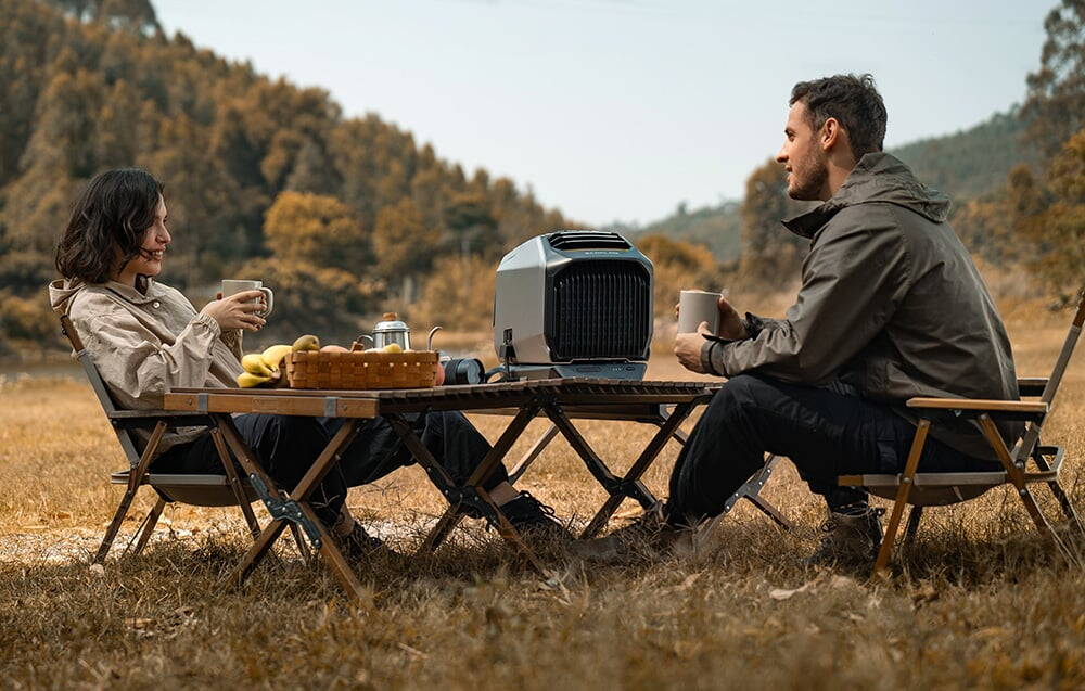 Cuplu la o masă cu un aparat de aer condiționat în timp ce face picnic într-un peisaj montan toamna