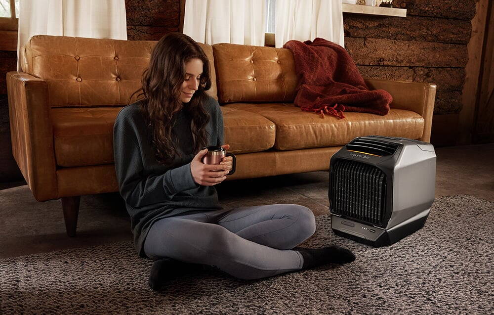Femeie stă pe podea cu o cană lângă un aparat de aer condiționat portabil într-o cameră de zi confortabilă