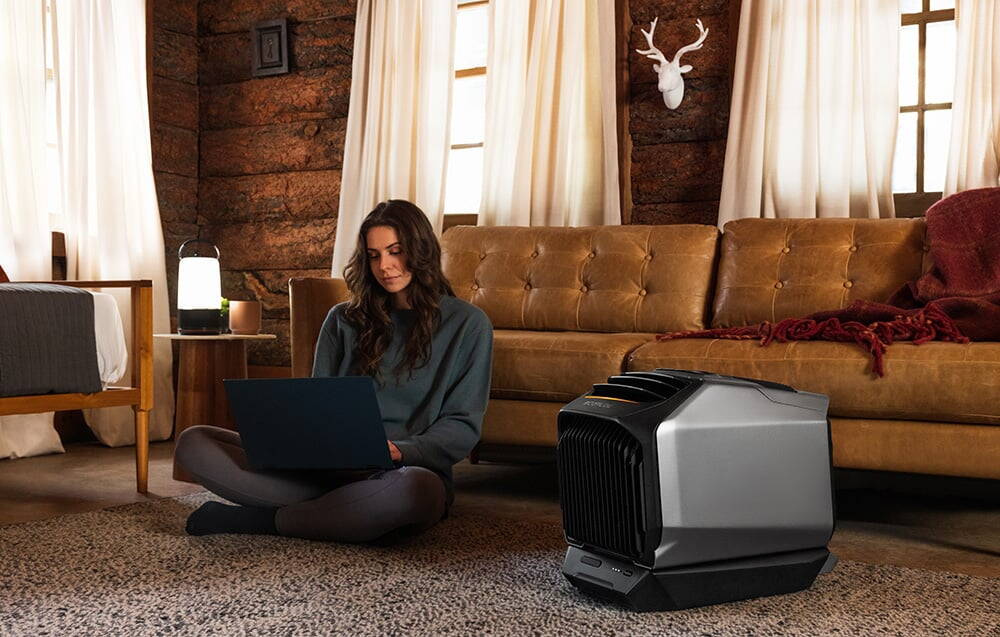 O femeie cu un laptop stă pe podea lângă un aparat de aer condiționat într-un interior rustic cu șemineu