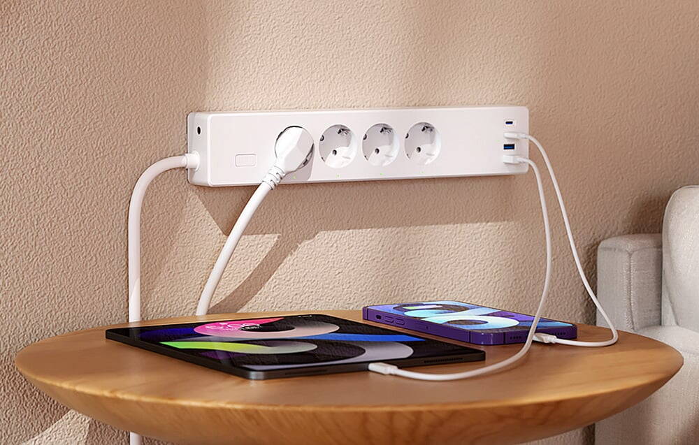 Bandă de alimentare albă cu trei dispozitive conectate așezate pe o masă rotundă, inclusiv un telefon și o tabletă